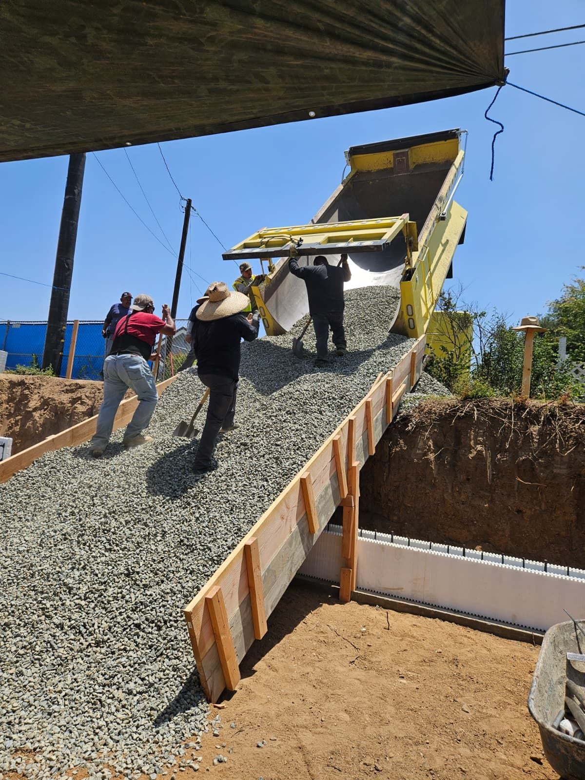 Dump truck placing gravel into foundation forms while the Mars Civil crew spreads it