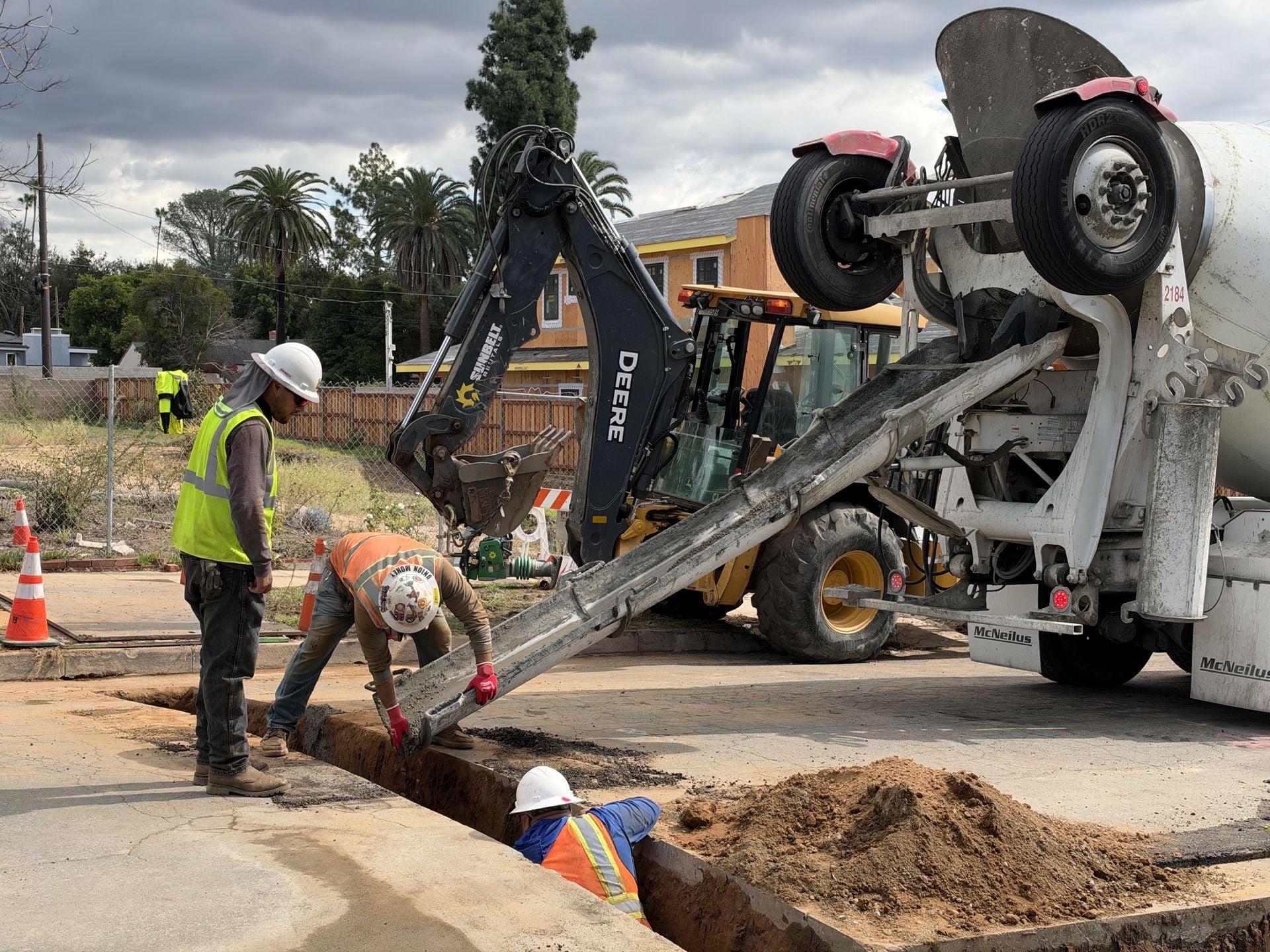 Mars Civil crew pouring concrete into a street trench with mixer truck and backhoe on site