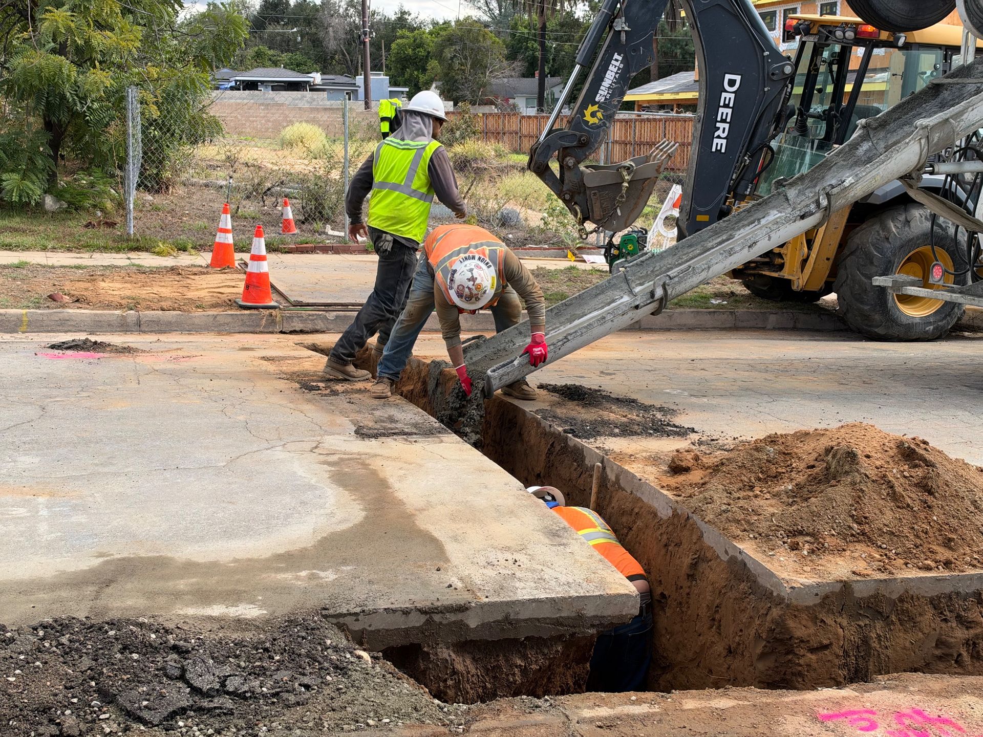 Workers placing concrete into a utility trench cut across a street