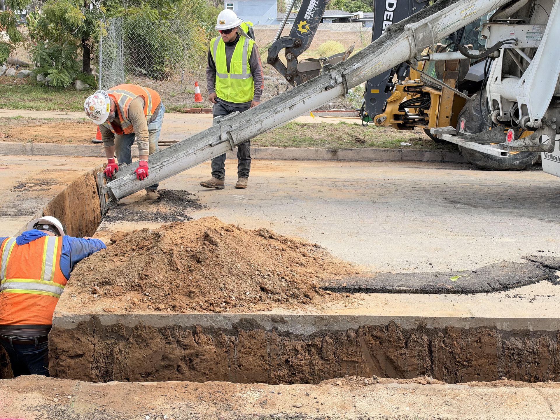 Crew guiding a concrete chute during a street trench pour